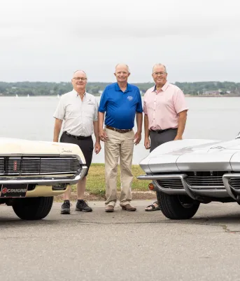 Three men standing between two heritage cars  