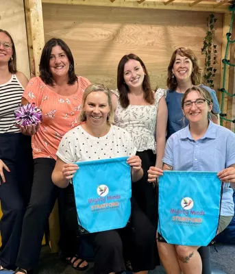 A group of women hold Might Minds bags in front of a rock-climbing wall.