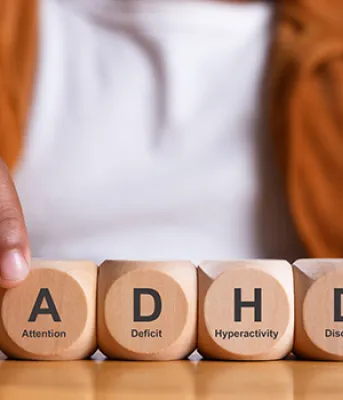Hands of person spelling ADHD with wooden blocks on a table