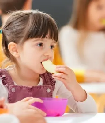 little girl sitting at a table eating a banana