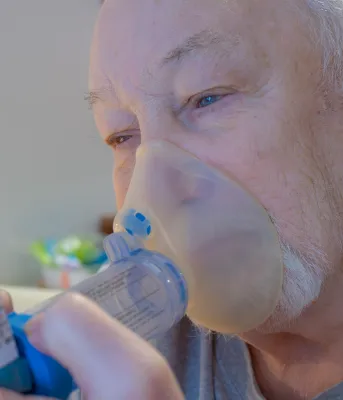 An older man uses an inhaler