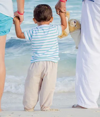 A man and a woman holds a child&#039;s hand while watching the waves come in at the beach