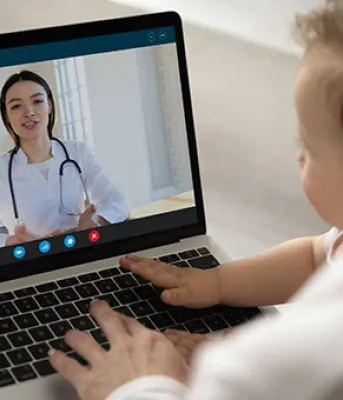 photo of a woman with baby on a couch having a video call on her laptop computer with a doctor
