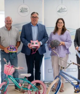 Communities receive funding for active transportation projects image of four people standing shoulder to shoulder inside a room in front of a display banner each holding a cycling helmet