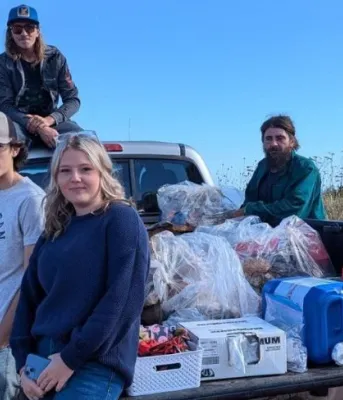 Eastern watershed group boosts biodiversity and community pride image of a group of people siting on and standing around a truck parked near the shore