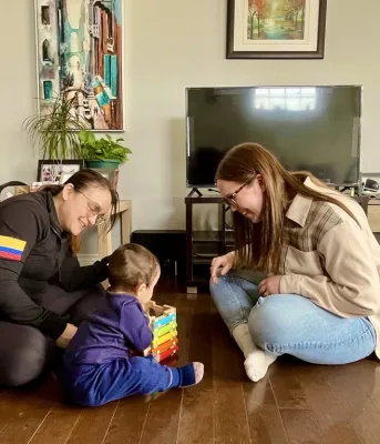 Two adults sit on either side of a toddler, smiling