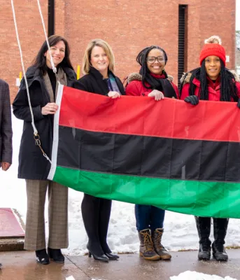 Statement by Premier Dennis King for Black History Month image of a group of people standing shoulder to shoulder holding a flag before it is raised up a flagpole