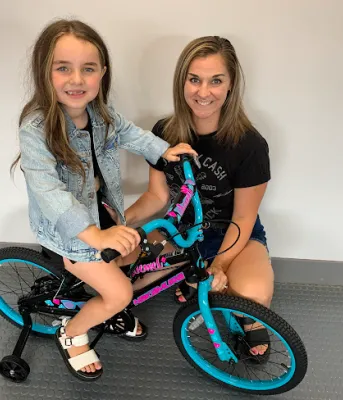 Bike rebate seals the deal for a special birthday present image of a young person on a bicycle with training wheels and an adult kneeling behind