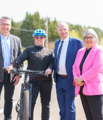 image of four peole standing shoulder to shoulder beside a road and one person holding onto a bicycle