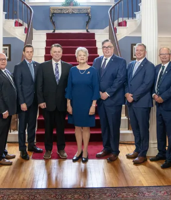 image of a group of people standing shoulder to shoulder inside a stately room in front of stairs