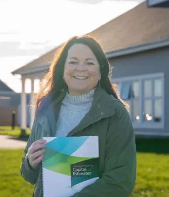 image of a person holding a booklet in front of her with a home in the background