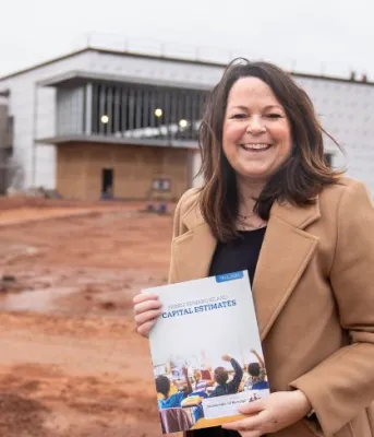 image of a person holding a document while standing in front of a building under contruction