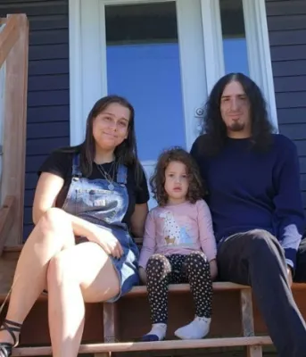 A sense of community and pride image of two adults and a child sitting on the stairs of a porch in front of a house