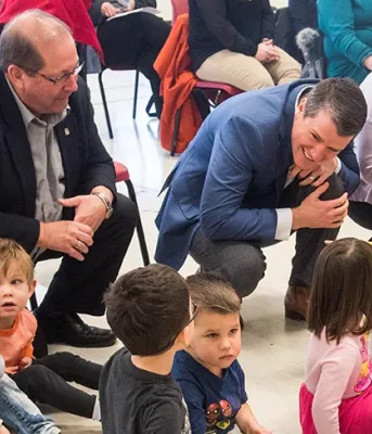 Three adults crouch on the floor where day care children are sitting