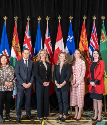 image of six people standing shoulder to shoulder in front of Canada&#039;s provincial flags