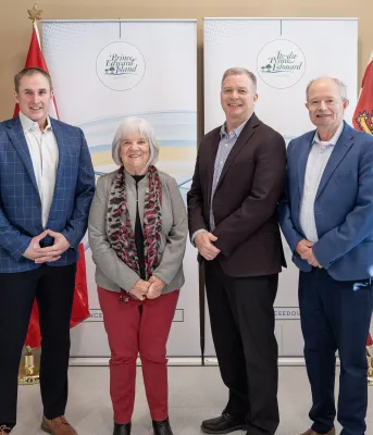 Access PEI director Mark Arsenault, Cornwall Mayor Minerva McCourt, Minister of Health and Wellness and Cornwall-Meadowbank MLA Mark McLane, and Minister of Transportation and Infrastructure Ernie Hudson Four people standing in a room smiling, next to Access PEI sign