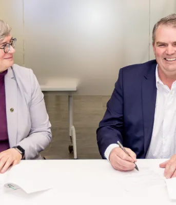 Dr. Heather Bruce et le ministre Thompson sont assis l'un à côté de l'autre en train de signer des documents.