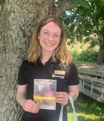 Learn how to protect your property from wildfires image of a person standing in the shade in front of tree and holding a brochure