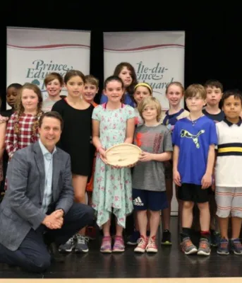 Minister Brad Trivers kneels in front of a group of children from Spring Park School's Grade 4C French Immersion class