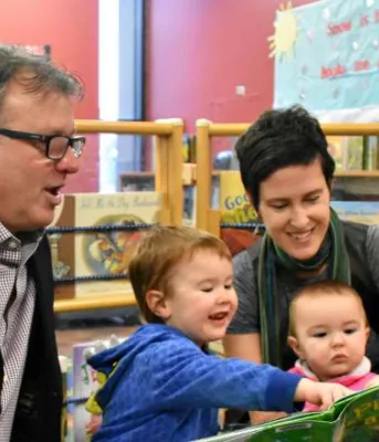 Minister Doug Currie reads a story with Charlie and Rosie and their mother Jinny Greaves.