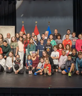 image of a large group of young students and some adults on a performance stage with flags in the background