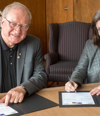 Two people sitting at a desk signing an official document