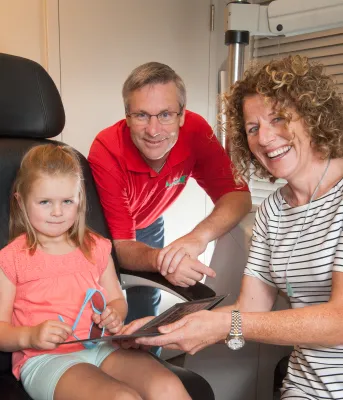 Minister Henderson, and Dr. Toombs are showing a little girl some eye glasses.