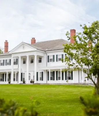 image of a large stately home with a large grass area and various trees surrounding it.