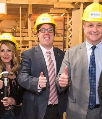Five people standing side by side wearing hard hats and holding their thumbs up