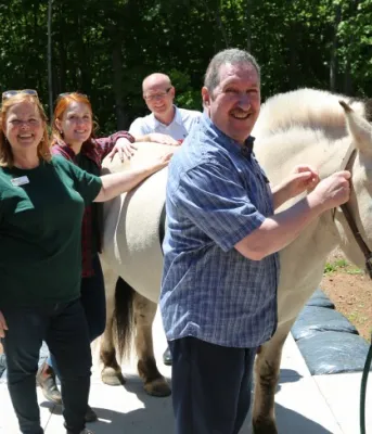 Billy the horse stands outside on a spring day with five people petting him