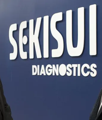 Sekisui Diagnostics expanding again and adding more jobs Two people standing in front of a sign at Sekisui Diagnostics