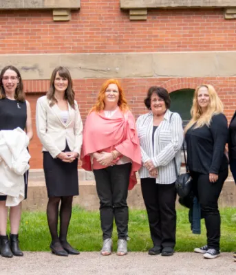 Investing in Island women and girls image of a group of people standing shoulder to shoulder in front of a red brick building