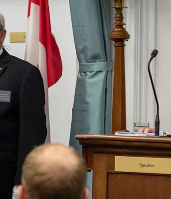  image d&#039;une personne lisant un discours assis derrière un podium et deux personnes regardent à côté de l&#039;orateur