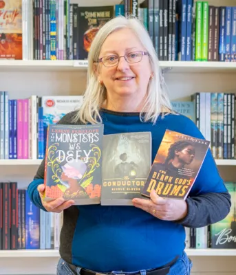 Book club celebrating Black authors image of a person in a bookstore standing in front of bookshelves holing three books