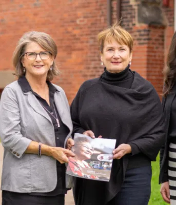 Long term care review identifies recommendations for enhancement four people standing shoulder to shoulder in front of a brick building with two of them holding a booklet