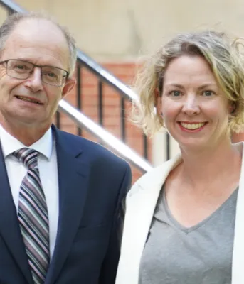 a woman and a man standing beside each other in front of a brick building