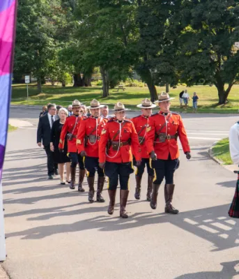 Accession proclamation ceremony held at Government House image of a bagpiper leading a procession past a gate with trees in the background