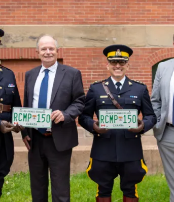 image of four people standing shoulder to shoulder in front of a building and holding a license plate