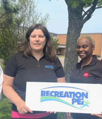 Recipients of the Anti-Racism Microgrants image of four people standing shoulder to shoulder holding a small sign with a tree and building in the background
