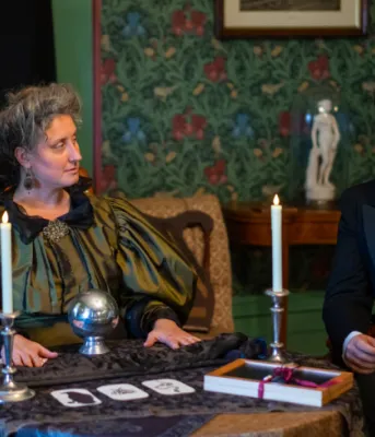 Halloween events planned for Museum and Heritage Foundation image of two people dressed in 1800s clothing siting at a table with candles and cards on it
