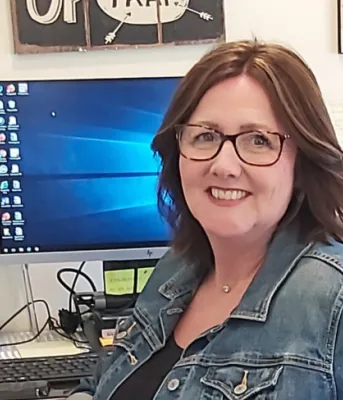 Youth Worker Spotlight: Karrie MacDougall image of a woman sitting at her work desk with computer screen in the background
