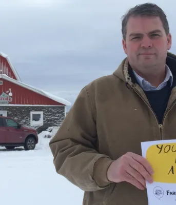 Image of Minister Bloyce Thompson in front of his barn holding a Farmers Talk sign that reads &quot;You are not alone&quot;