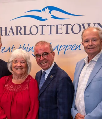 image of  a group of six people standing shoulder to shoulder in front of a City of Charlottetown sign