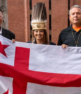 Province celebrates Treaty Day image of three people standing shoulder to shoulder holding a flag in front of them