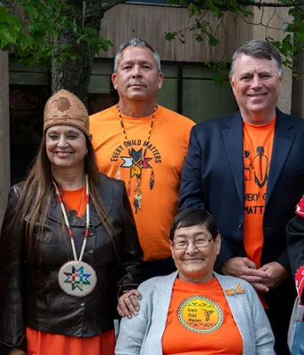 Recognition of National Day for Truth and Reconciliation image of a group of people some in colourful ceremonial clothing standing shoulder to shoulder in front of a building