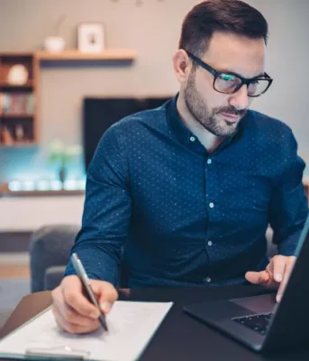 man looking at a computer and writing something down on a notepad