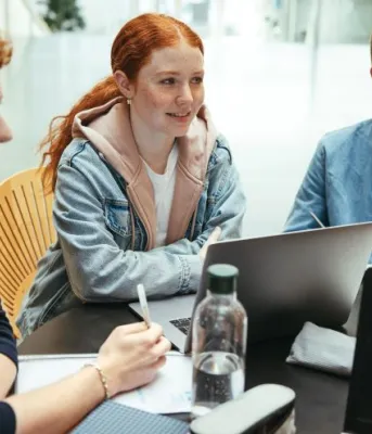 three young adults sitting at a table in front of a computer